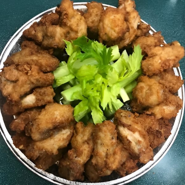 A platter of golden-brown fried chicken pieces arranged around a pile of fresh green celery sticks.