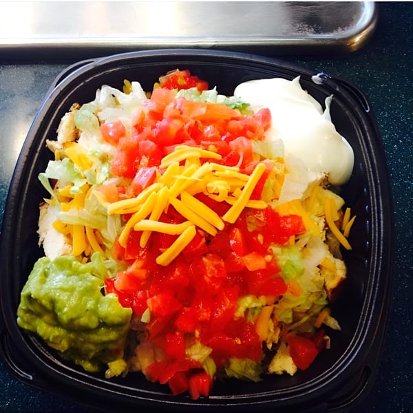 Grilled chicken salad with lettuce, tomatoes, shredded cheese, guacamole, and sour cream in a black bowl.