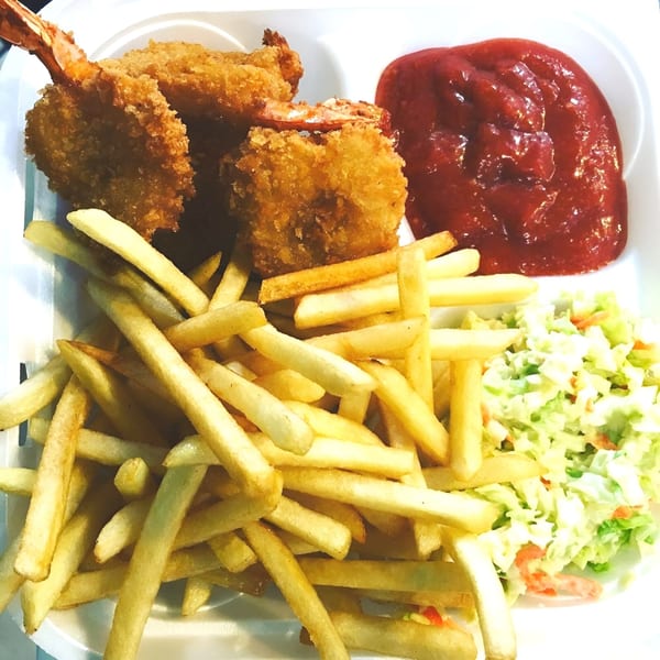 Fried shrimp, french fries, coleslaw, and ketchup served in a white takeout container.
