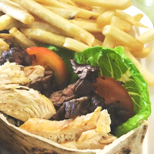 Grilled chicken and beef shawarma in pita bread with lettuce, tomatoes, and a side of fries.