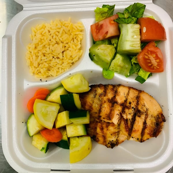 Grilled chicken, rice, mixed vegetables, and a side salad in a white takeout container.