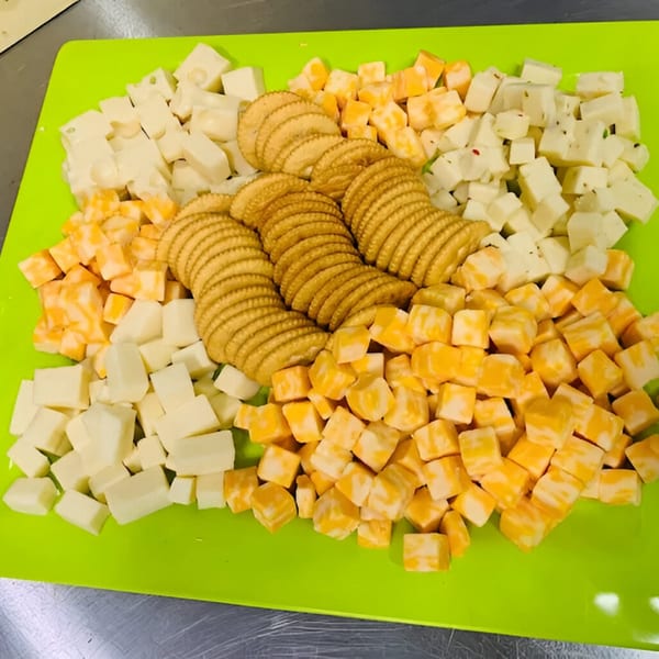 A bright green cutting board holds three rows of crackers surrounded by cubed white and orange cheese.